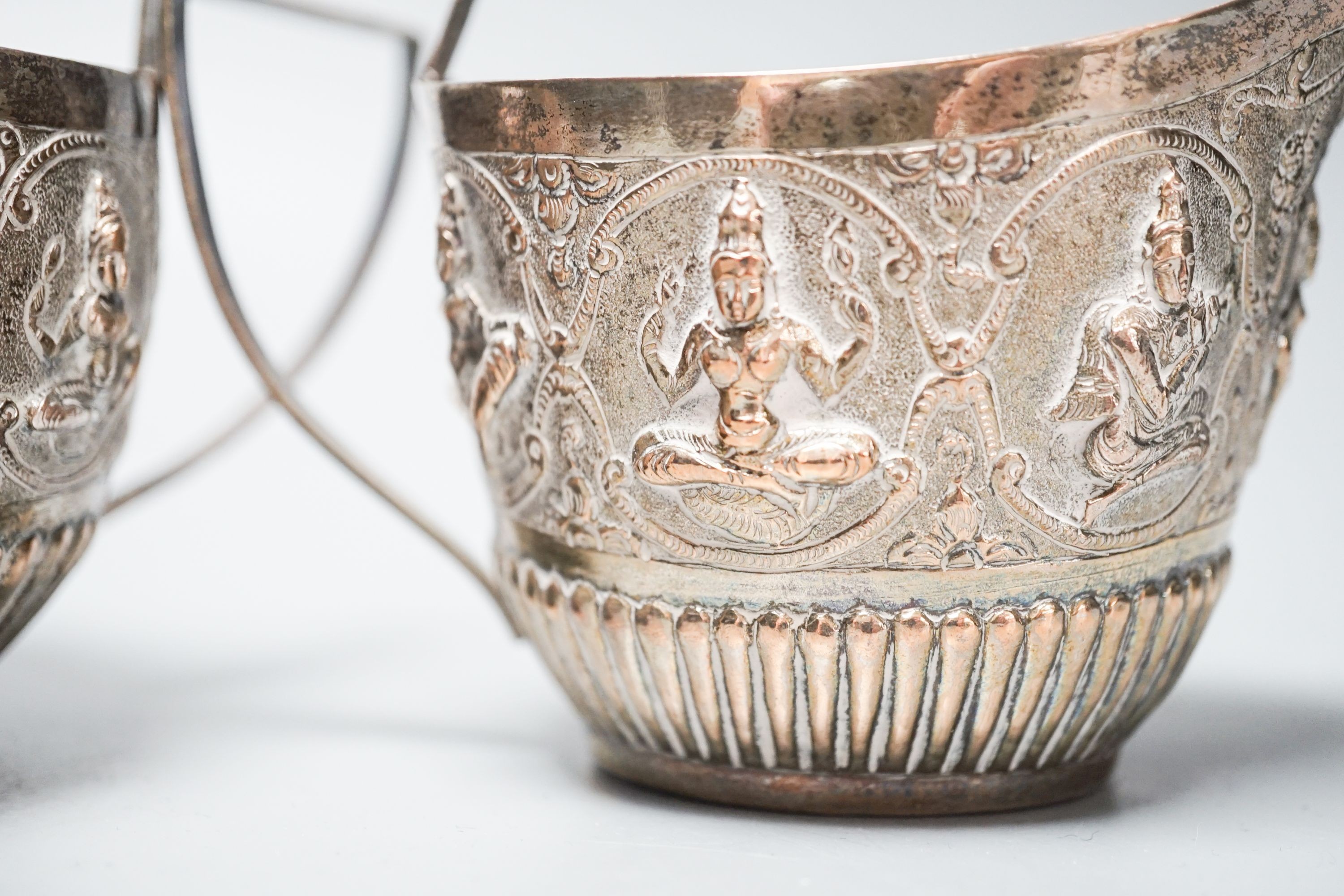 An Indian white metal sugar bowl and cream jug, embossed with deities, 8.5oz.